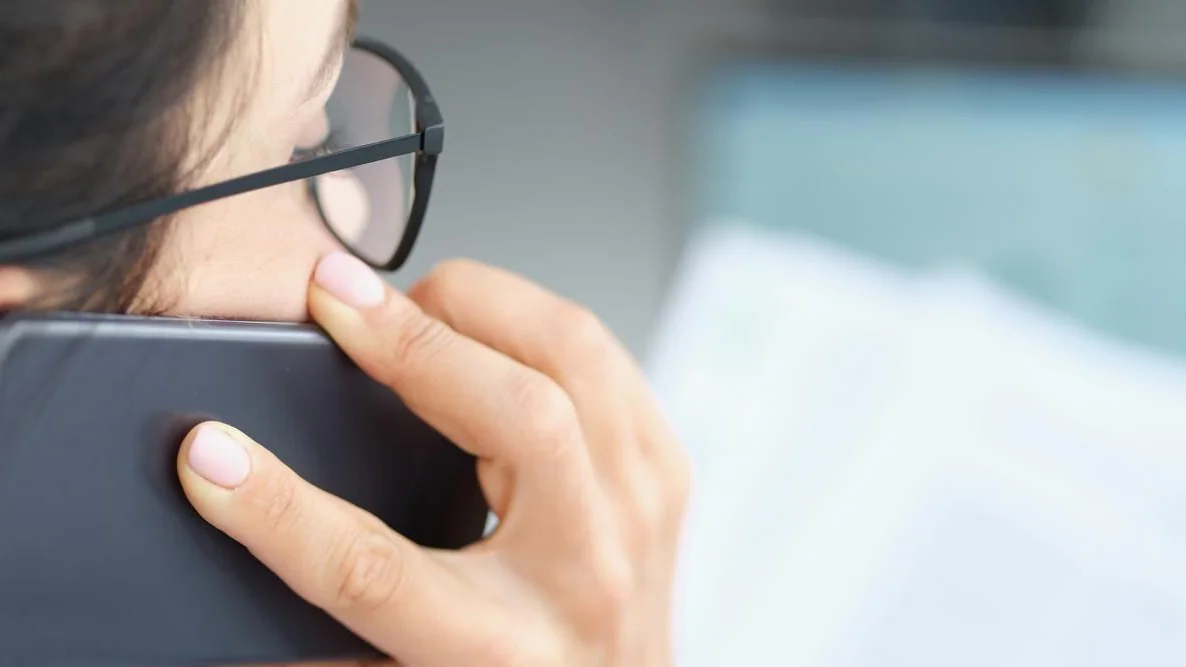 Person pratar i telefon och granskar ett dokument, illustration till regler om telefonförsäljning och skriftligt avtal