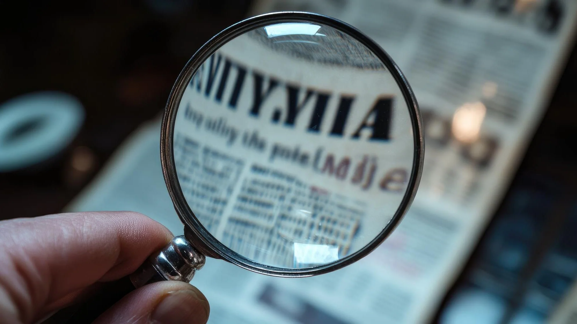 Hand granskar en tidning genom ett förstoringsglas som symbol för källkritik och faktakontroll